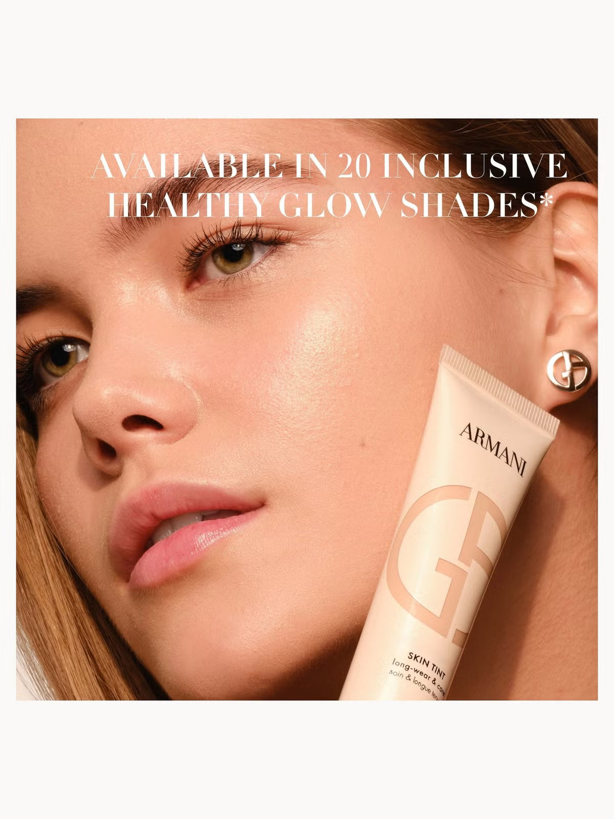 A close-up beauty ad showing a woman's face and ear with a tube of Armani GF Skin Tint held near her cheek. White text across the top reads, 'AVAILABLE IN 20 INCLUSIVE HEALTHY GLOW SHADES*'.